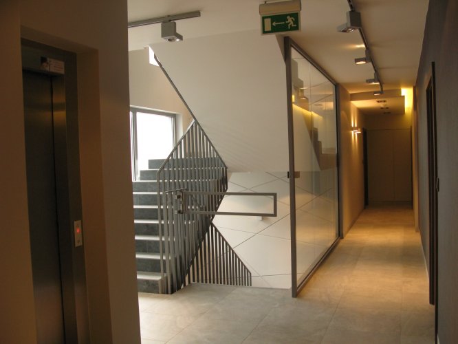 Budynek B - wewnęrzny korytarz na poziomie parteru, widoczna klatka schodowa oraz winda z lewej strony.