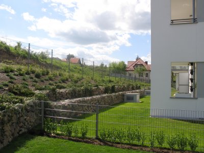 Budynek B - zielone ogródki i tarasy mieszkań parterowych, w tle widoczna zieleń osiedlowa.