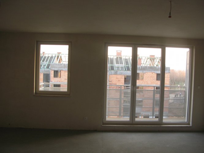 Widok z pokoju dziennego mieszkania w budynku 15, przez potrójne okna balkonowe na powstający budynek 16.