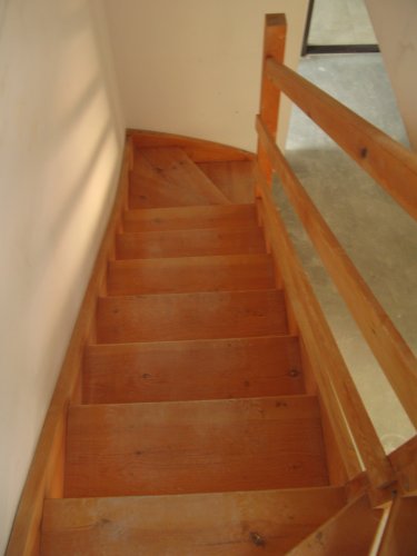 Drewniane schody w mieszkaniu 2-poziomowym prowadzące z poziomu dolnego na poddasze ze skosami.