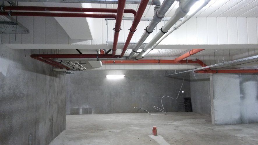 Budynek 2 - podziemna hala garażowa z wygodnymi miejscami parkingowymi, widoczne instalacje wodne mocowane pod sufitem.