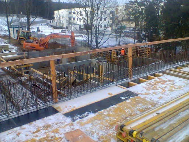 Budynek 2 - widok z piętra 1 w kierunku zachodnim z budynkiem 1, drogą, parkingiem i wjazdem na teren osiedla w tle.