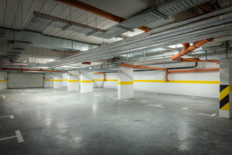 Budynek 1 - podziemna hala garażowa, widoczne szerokie miejsca postojowe oraz automatyczna brama wjazdowa.